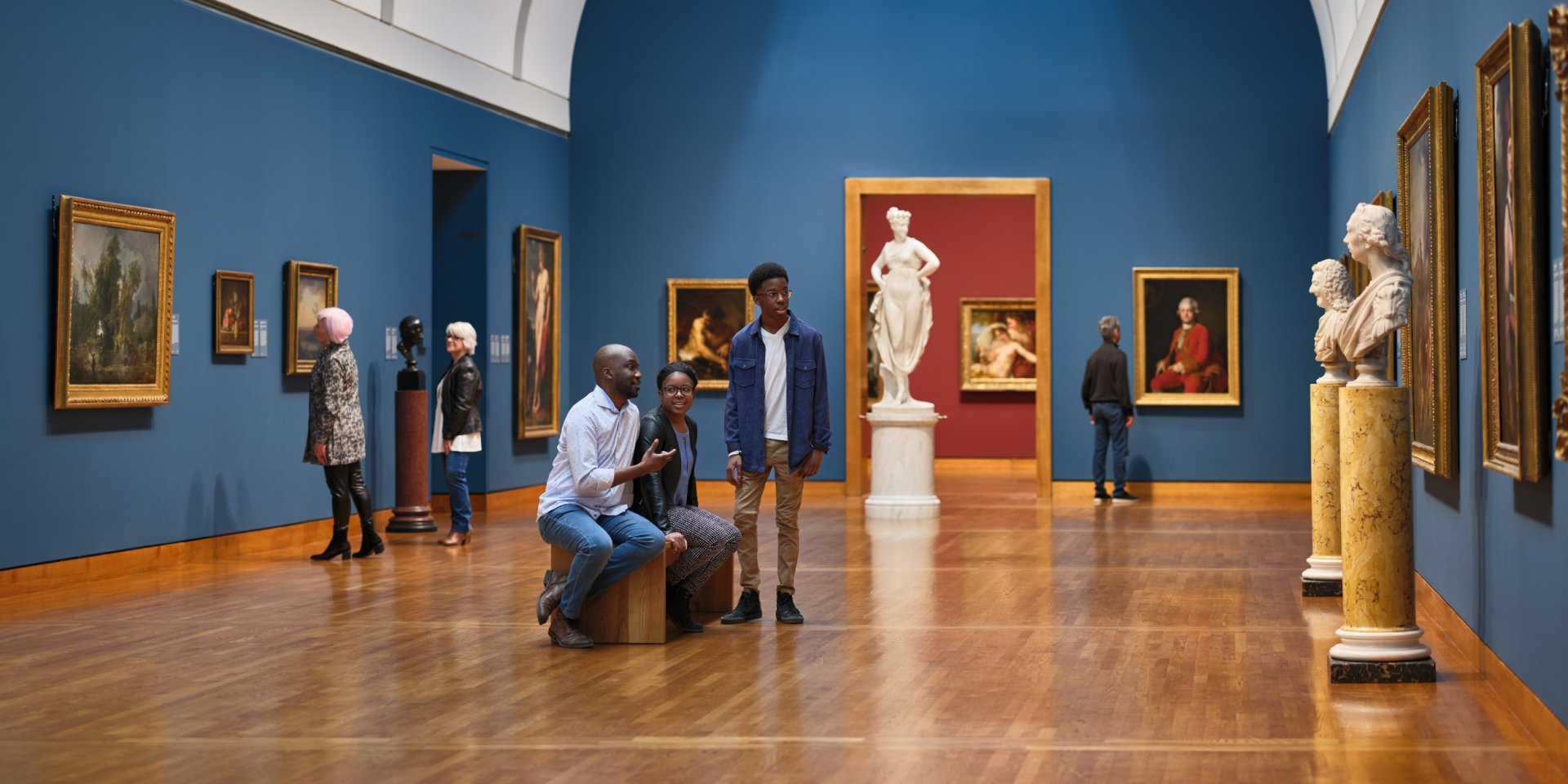 Visitors discussing and looking at paintings and sculptures in the European and American Galleries.
