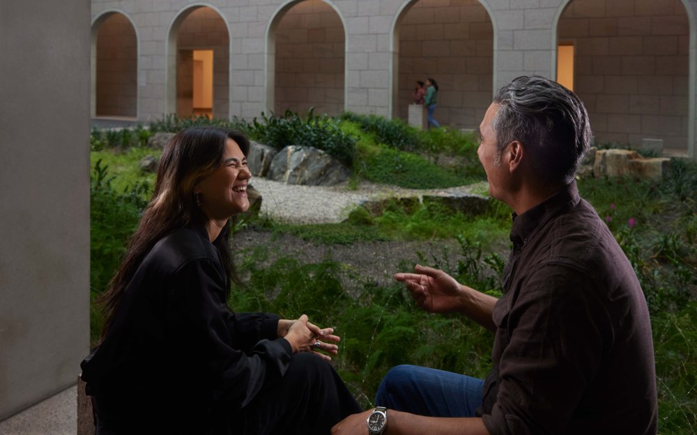 Two individuals looking at each other in a room with plants.