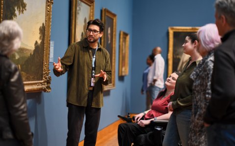 A man discusses an artwork with a group of adults.