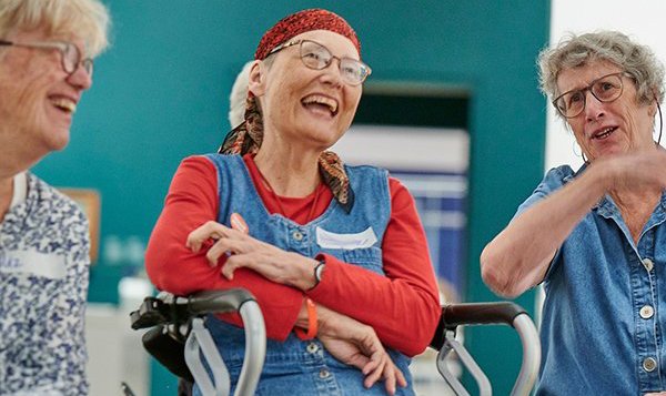 A woman gestures to a painting on a dark green wall as she discusses it with a group.